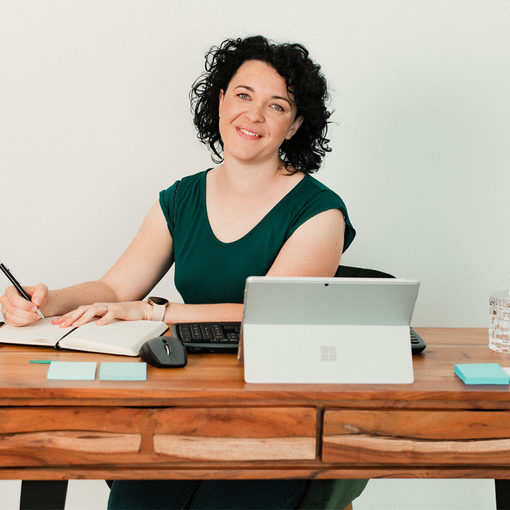 Paulina Hornbachner is sitting on her office desk, holding a pen and smiling into the camera